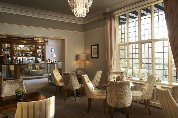 A well-lit room with a bar area, multiple chairs, and a large window with curtains.
