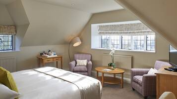 A bedroom with a bed, two armchairs, a desk, a lamp, and a window with a view.