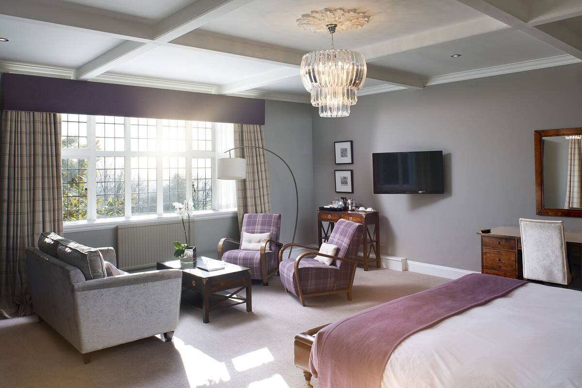 A bedroom with a bed, two armchairs, a sofa, a desk, a television, and a large window with curtains.