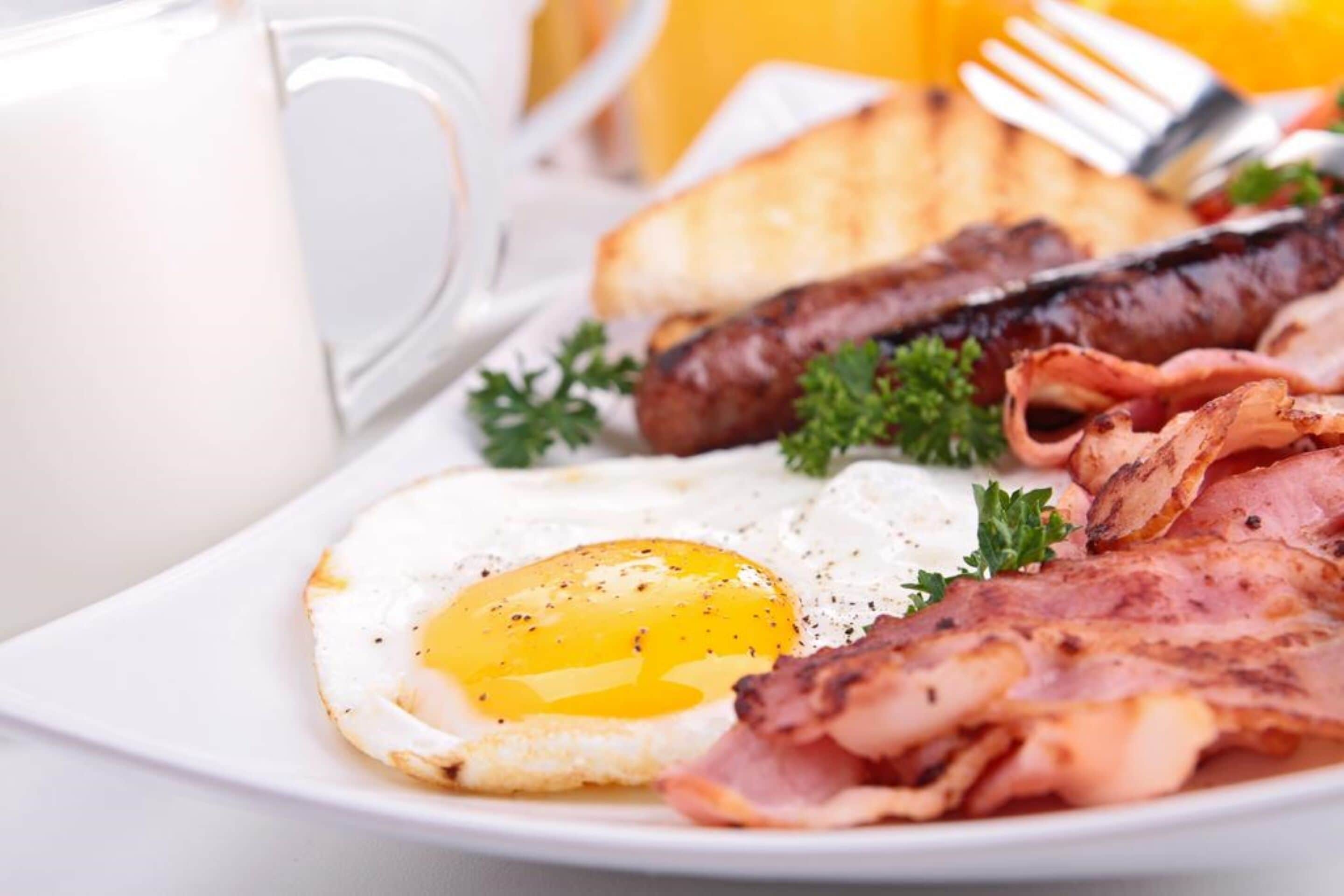 Ein Frühstücksteller mit Eiern, Speck, Würstchen, Toast und einem Glas Orangensaft.