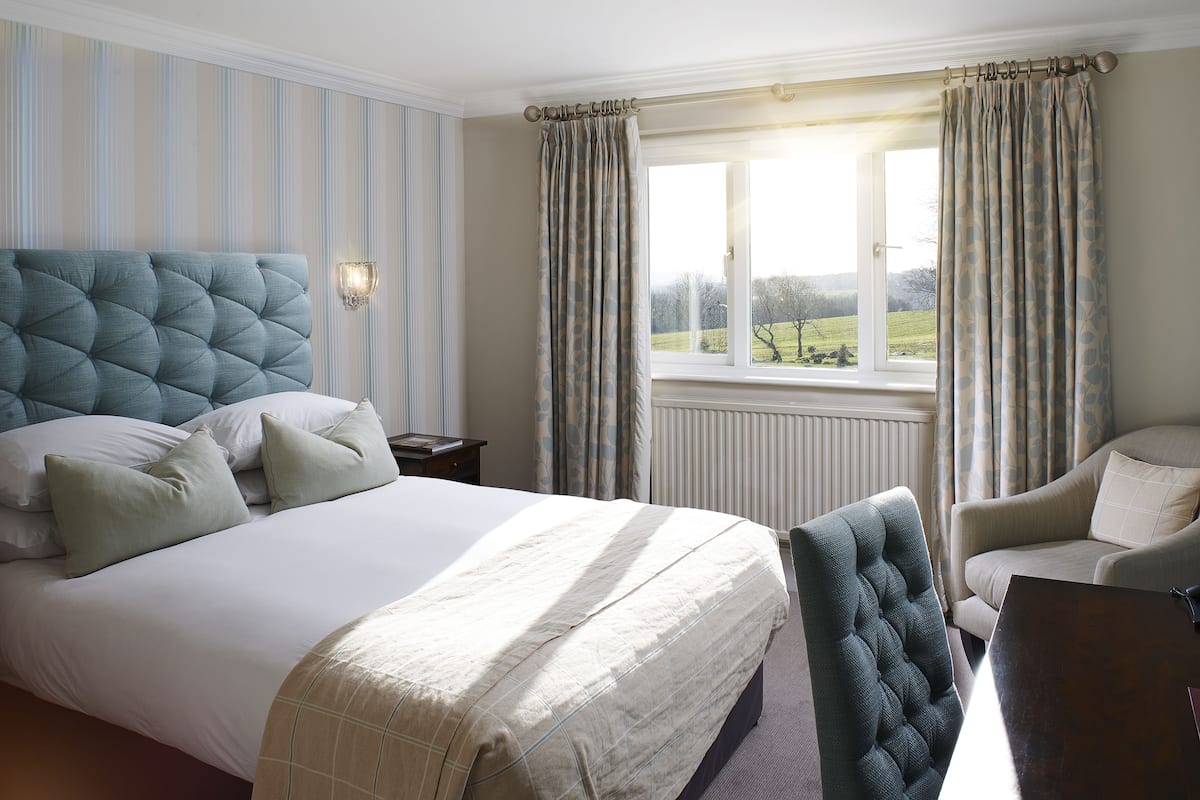 A bedroom with a large bed, a chair, a table, and a window with curtains.