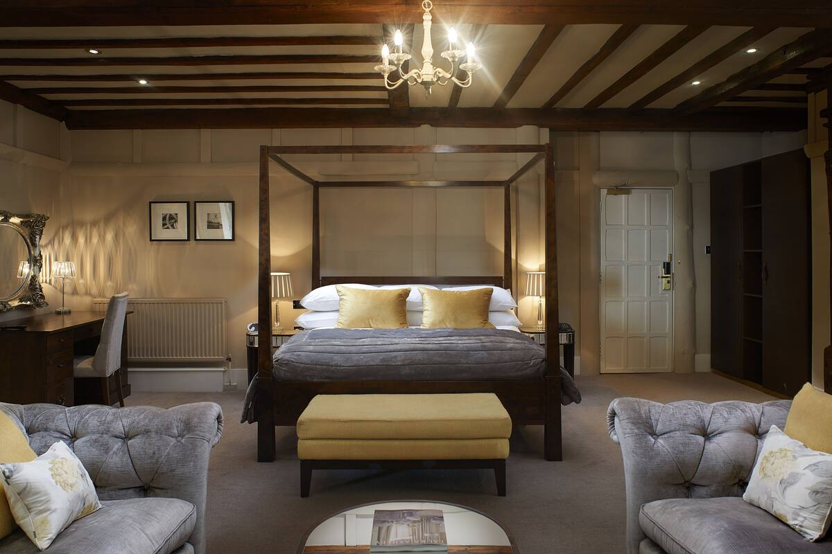 A bedroom with a four-poster bed, two bedside tables, a desk, and two armchairs.