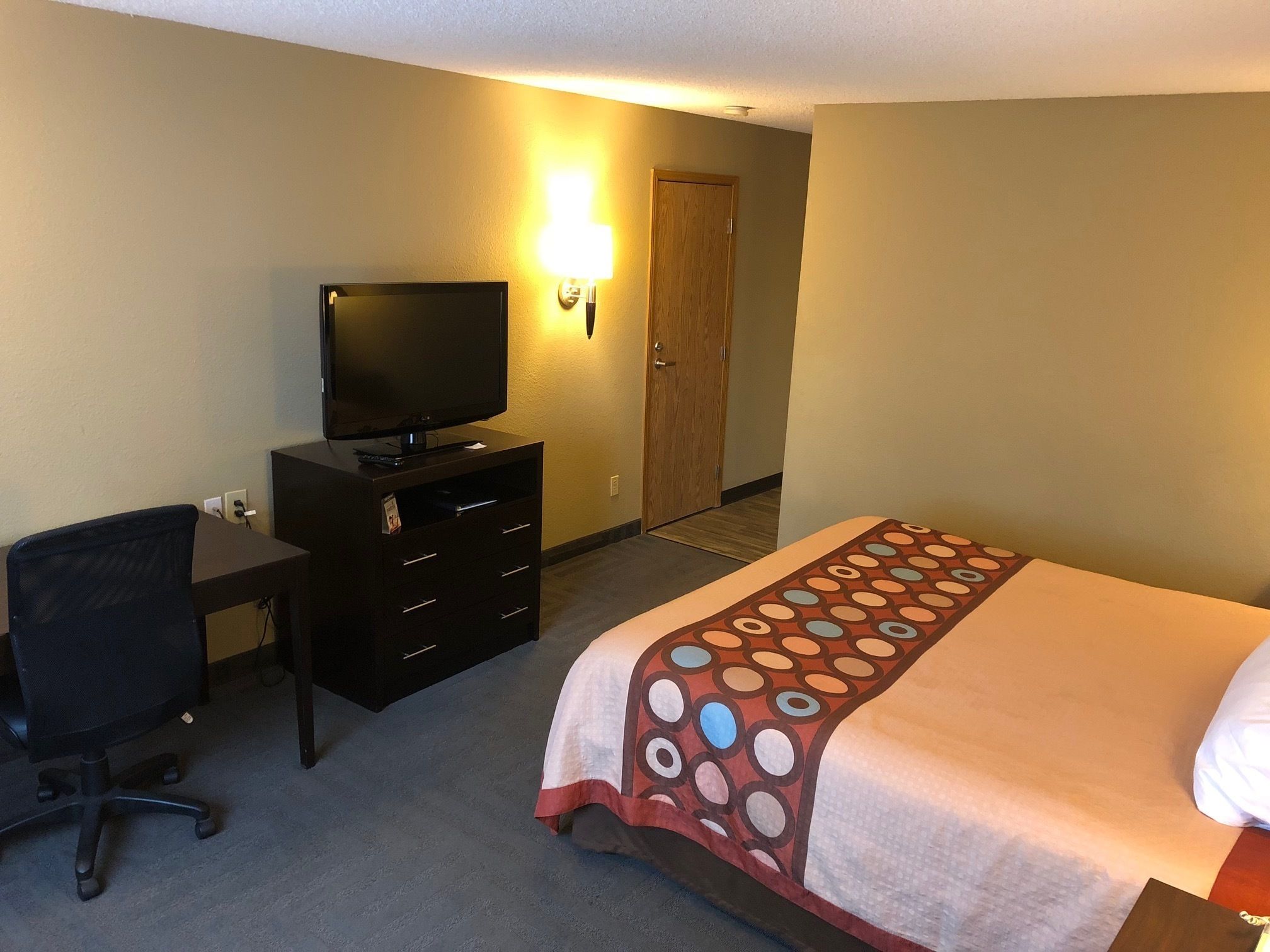 Una habitación de hotel con una cama, un escritorio con televisor y una silla.
