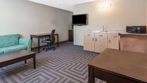 A hotel room with a green patterned sofa, a wooden desk, a television mounted on the wall, and a microwave on the countertop. - Super 8 by Wyndham LaGrande (La Grande)