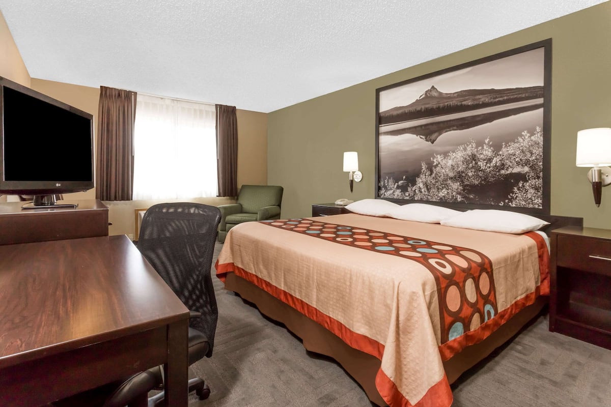 A hotel room with a bed, a desk, a chair, a television, and a painting on the wall.