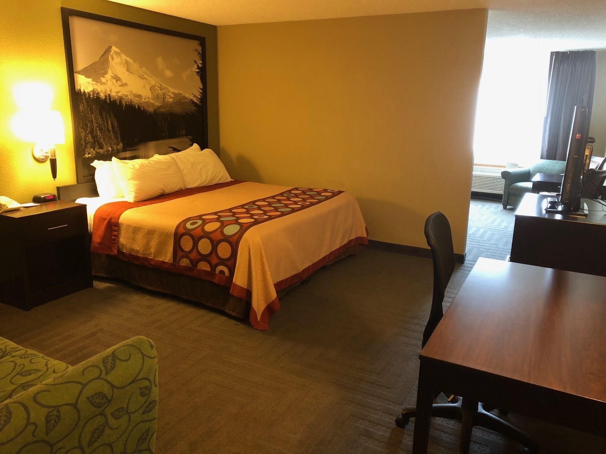 A hotel room with a bed, a desk, a chair, and a large framed picture on the wall.