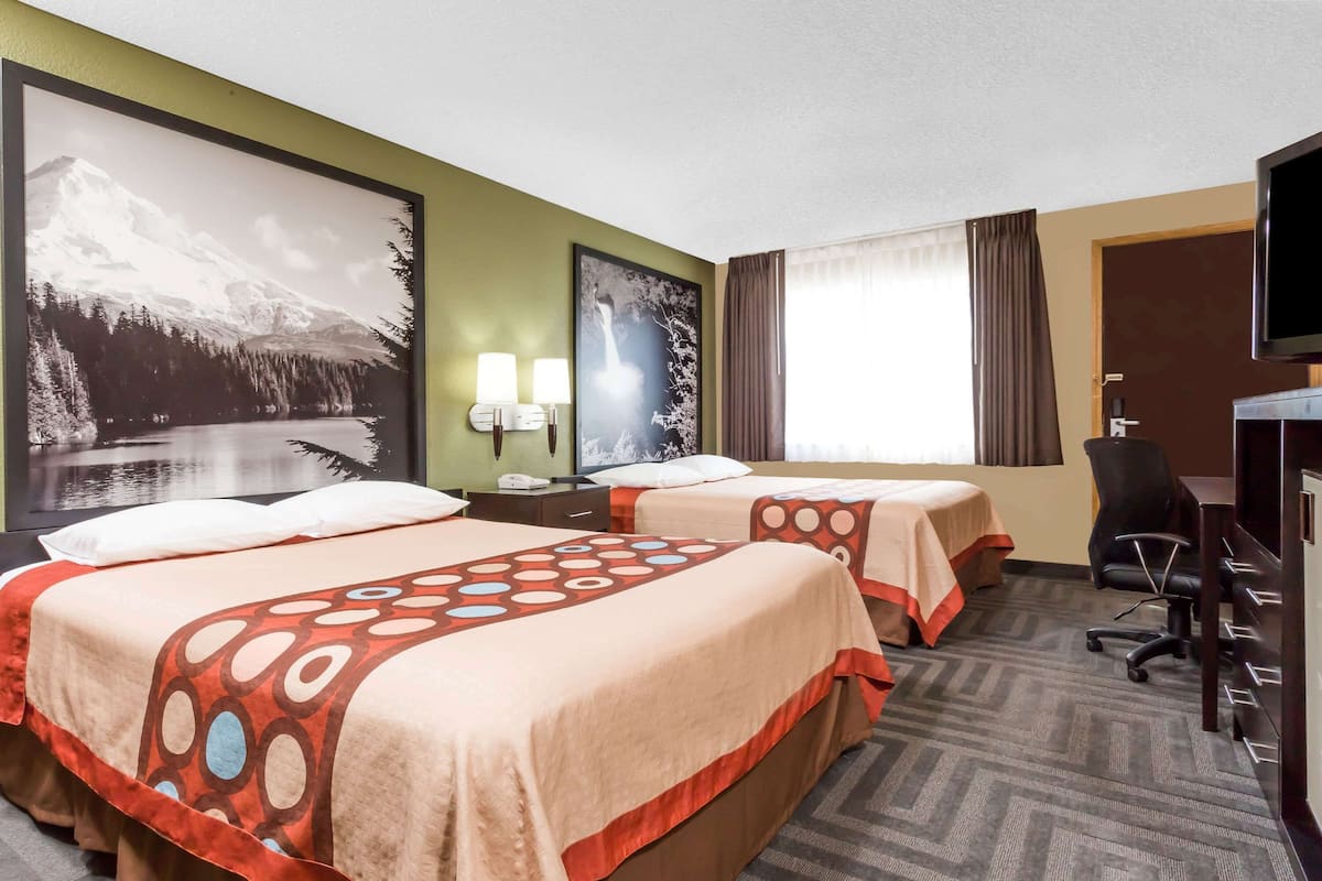 A hotel room with two beds, a desk, a chair, and a TV.