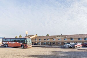 Un autobús estacionado frente a un motel, con varios vehículos y un cielo despejado.