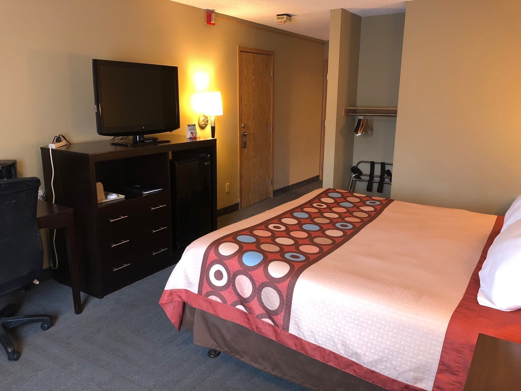 Une chambre d’hôtel équipée d’un lit, d’un bureau avec un ordinateur, d’une télévision et d’un porte-manteau.