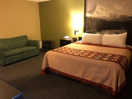 Una habitación de hotel con cama, sofá verde, mesita de noche y lámpara de pared.