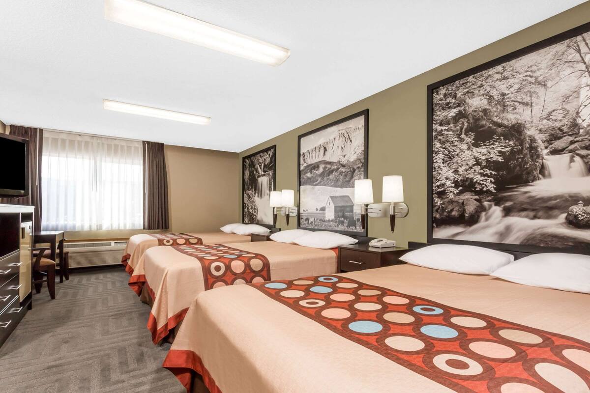 A hotel room with two beds, a desk, a television, and a large framed picture of a waterfall.