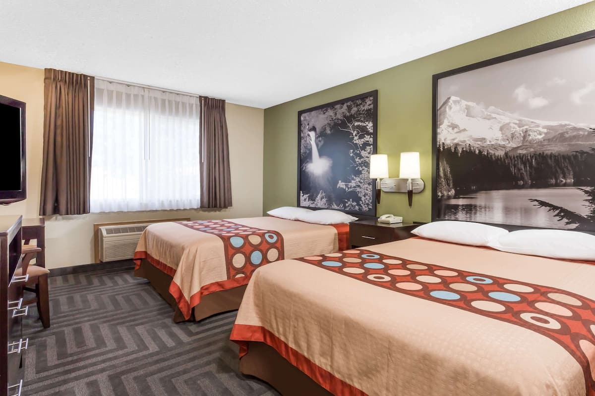 A hotel room with two beds, a TV, a desk, and a large window with curtains.