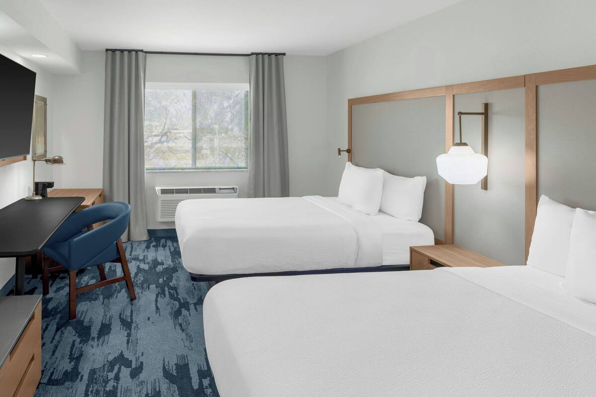 Een hotelkamer met twee bedden, een bureau, een stoel, een televisie en een raam met gordijnen.