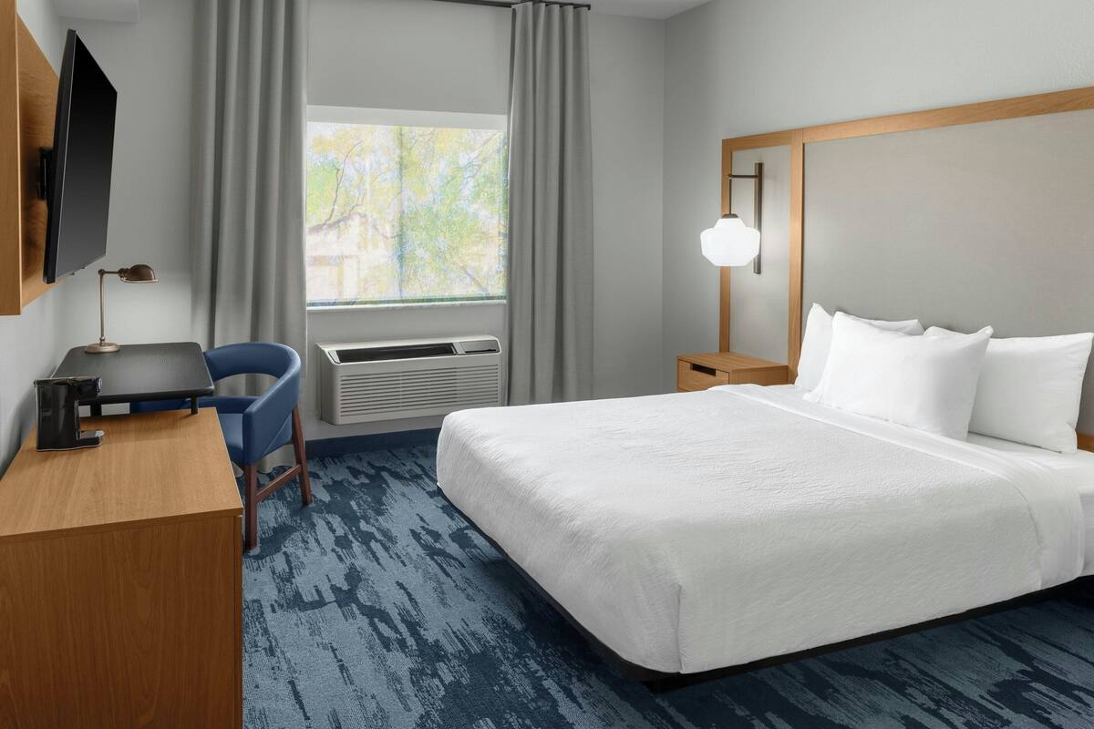 Een hotelkamer met een bed, een bureau, een stoel, een televisie en een raam met gordijnen.