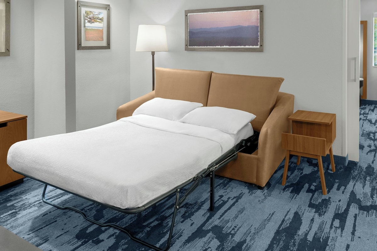 Een netjes ingerichte hotelkamer met een bed, nachtkastjes, een lamp en ingelijste foto’s aan de wand.