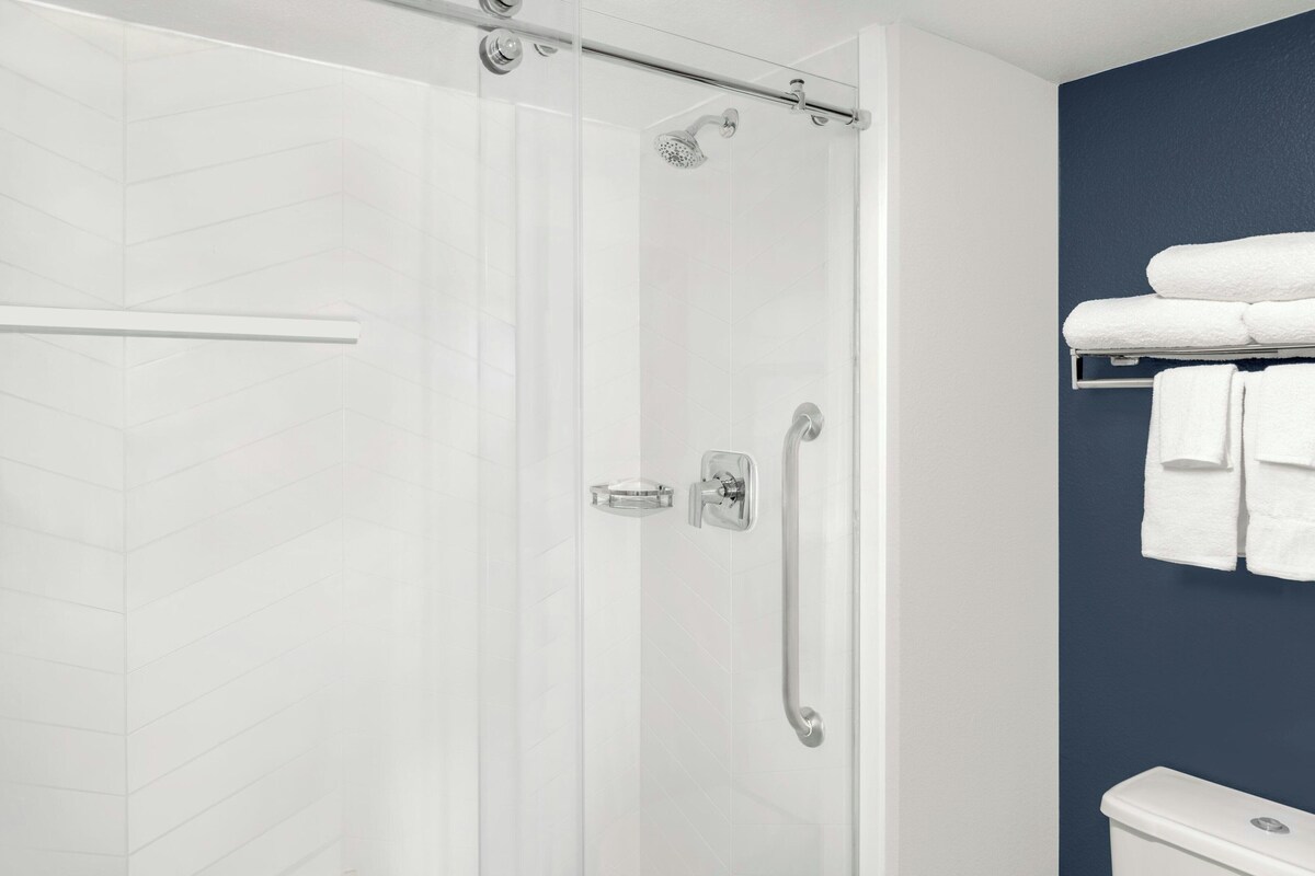 Un baño moderno con cabina de ducha de vidrio, pared revestida de azulejos blancos y una pared de acento azul oscuro.