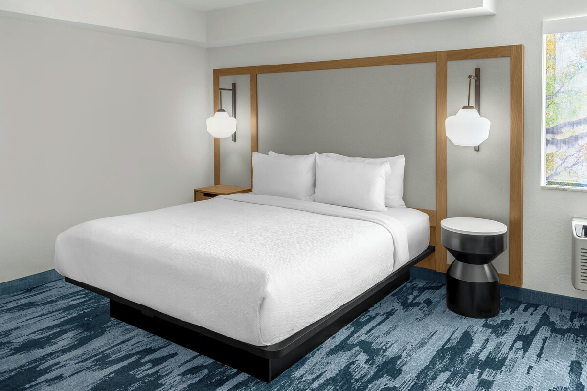A modern hotel room with a large bed, two bedside tables, and a unique wall-mounted light fixture.