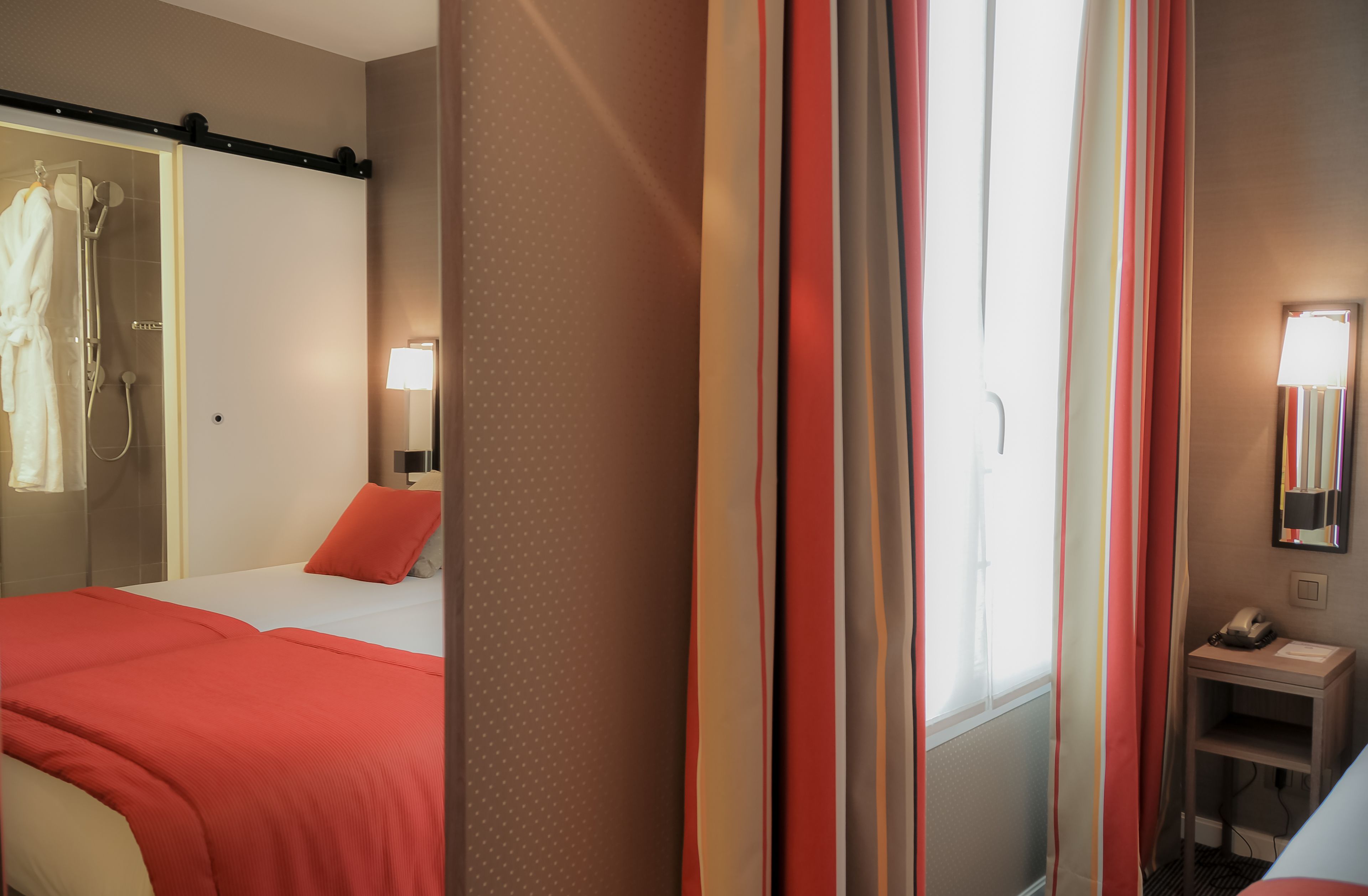 A hotel room with a bed, a bedside table with a lamp, a mirror, and a shower area.