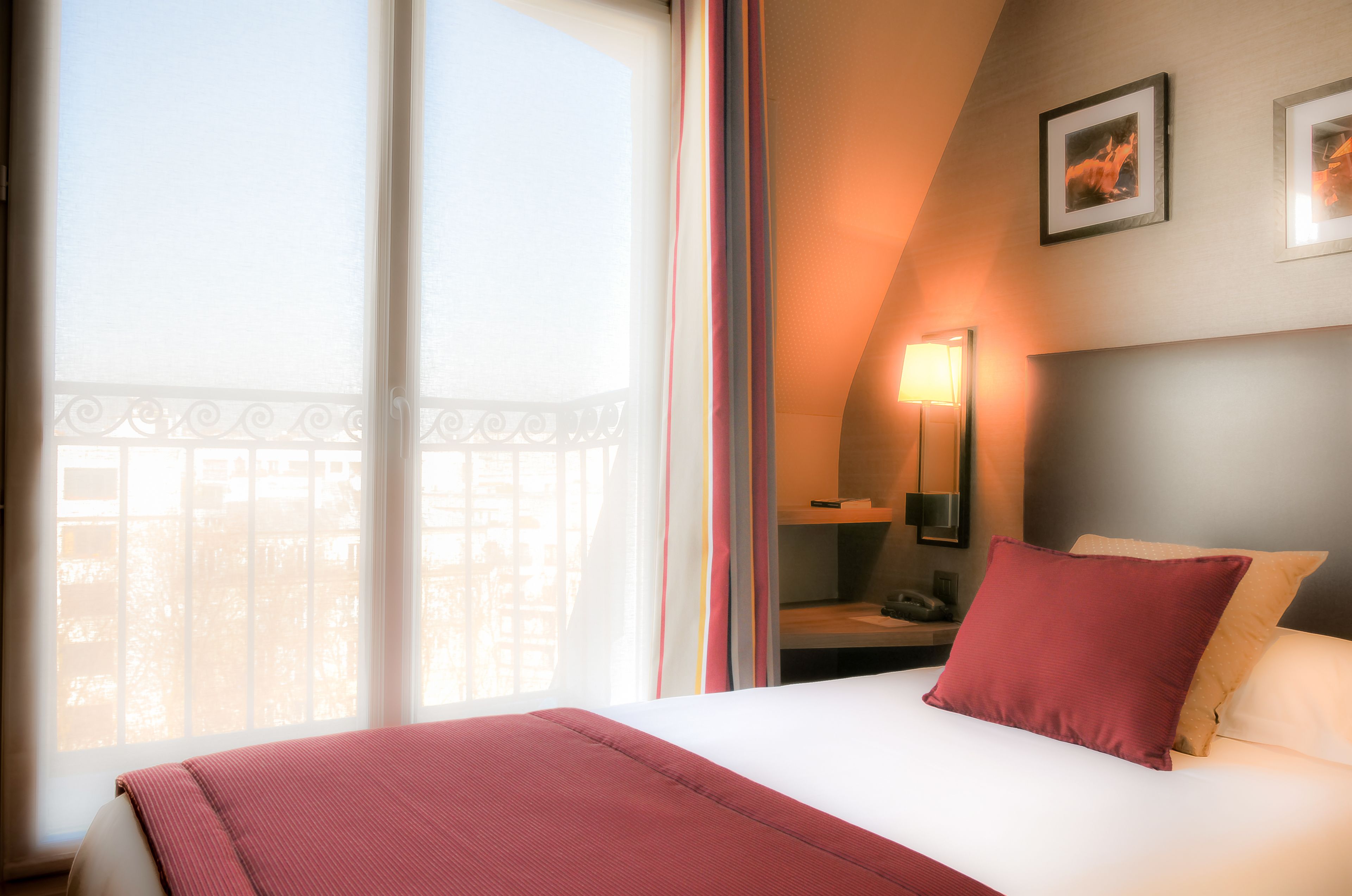 A hotel room with a large bed, a nightstand, a lamp, and a view of the outside.