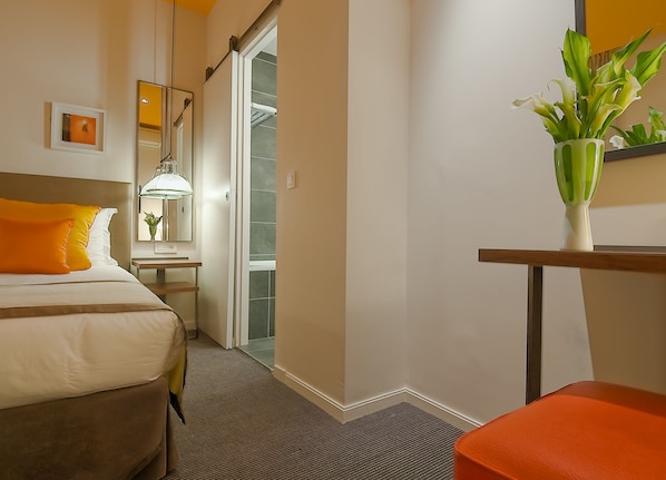 Una habitación de hotel con una cama, una mesita de noche, un espejo, una lámpara y una planta en maceta.