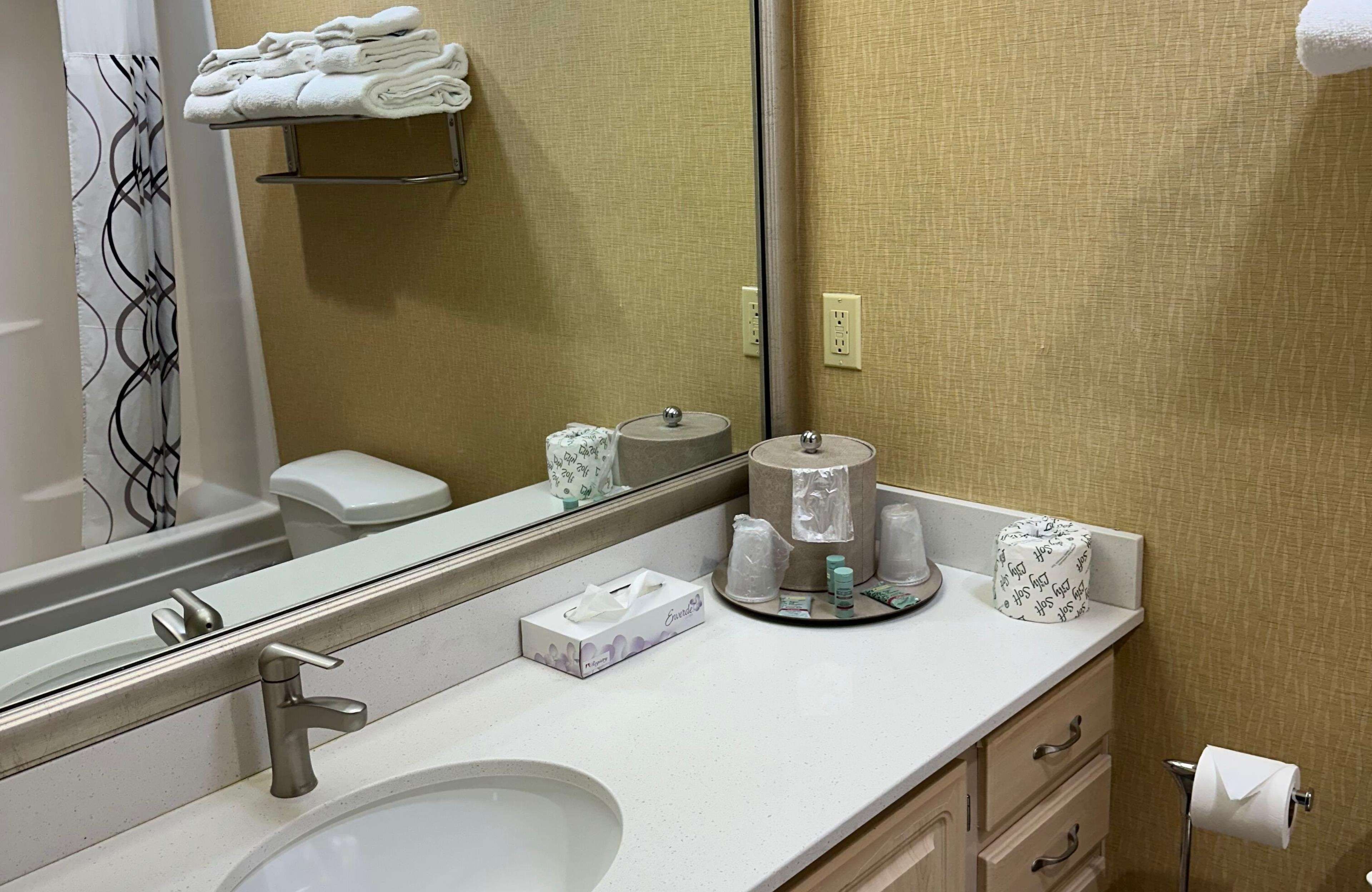 A hotel bathroom with a sink, mirror, towel rack, toilet, and a mirror reflecting the room.