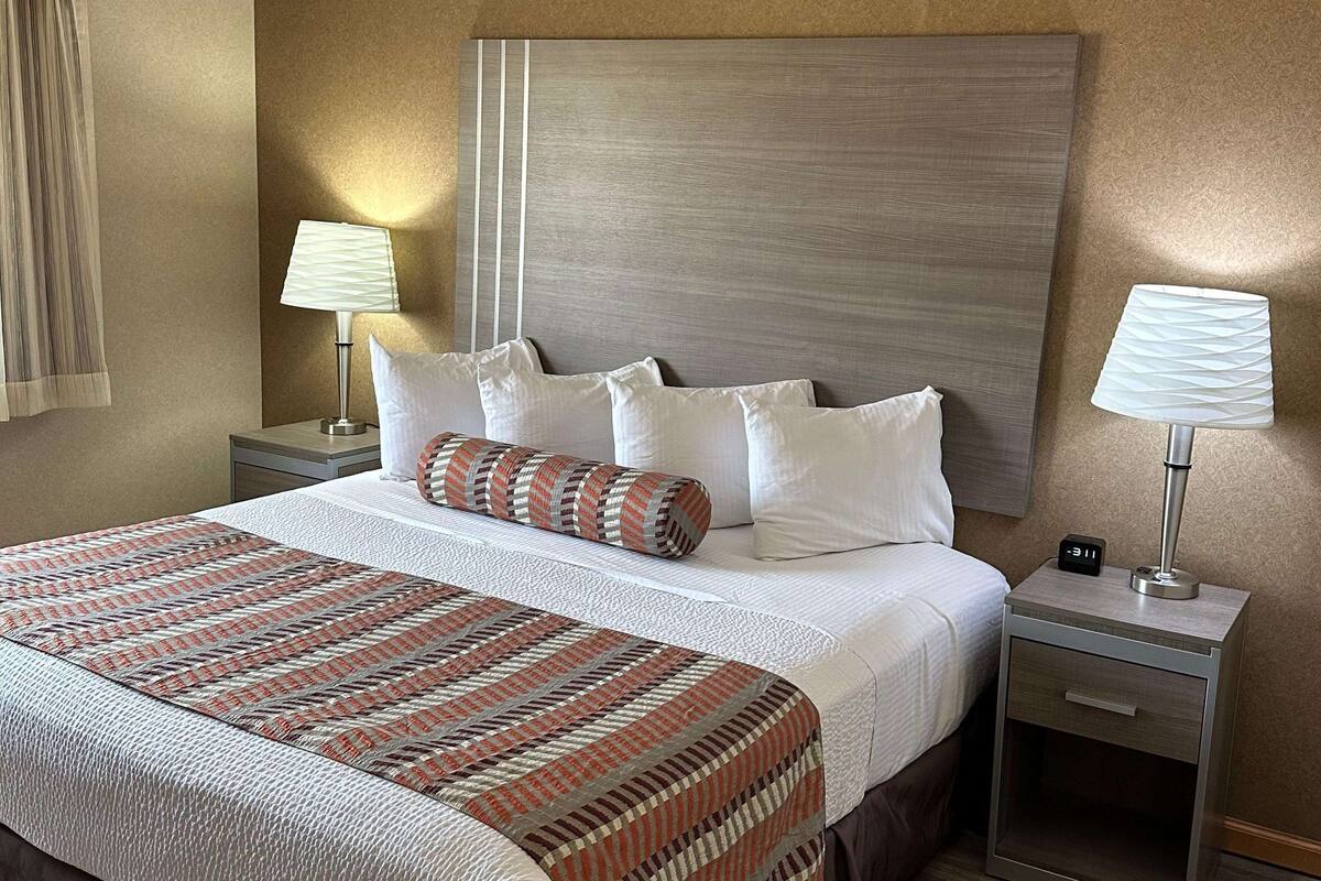 A hotel room with a large bed, two bedside tables, a nightstand, and a wall-mounted clock.