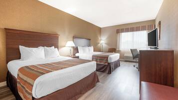 Ein Hotelzimmer mit zwei Betten, einem Schreibtisch, einem Stuhl, einem Fernseher und einem Vorhangfenster.