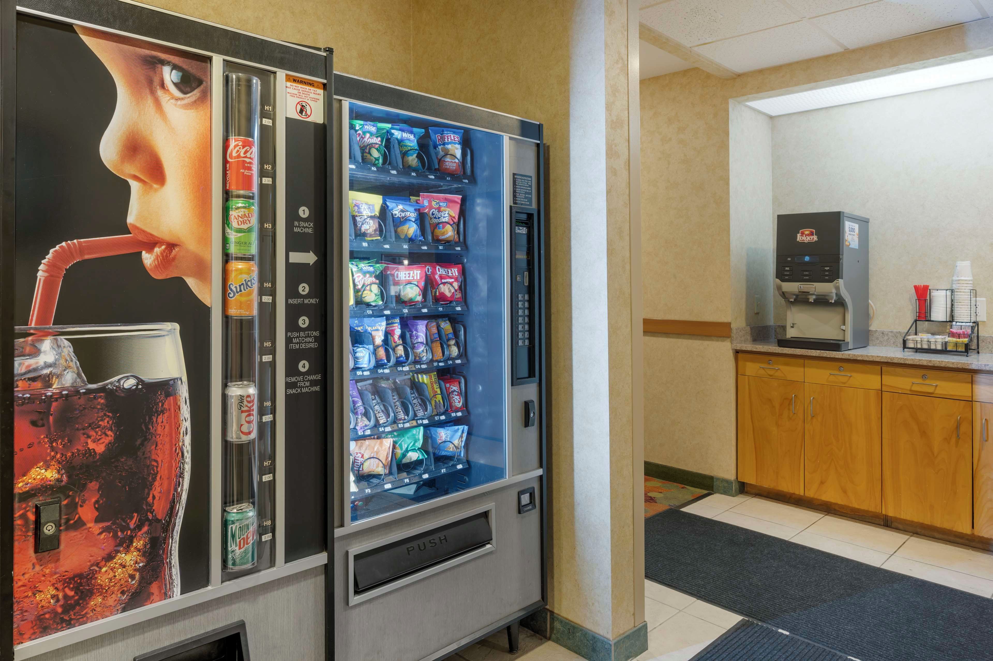 Máquina expendedora con diferentes snacks y bebidas, una cafetera y un microondas en una habitación de hotel.