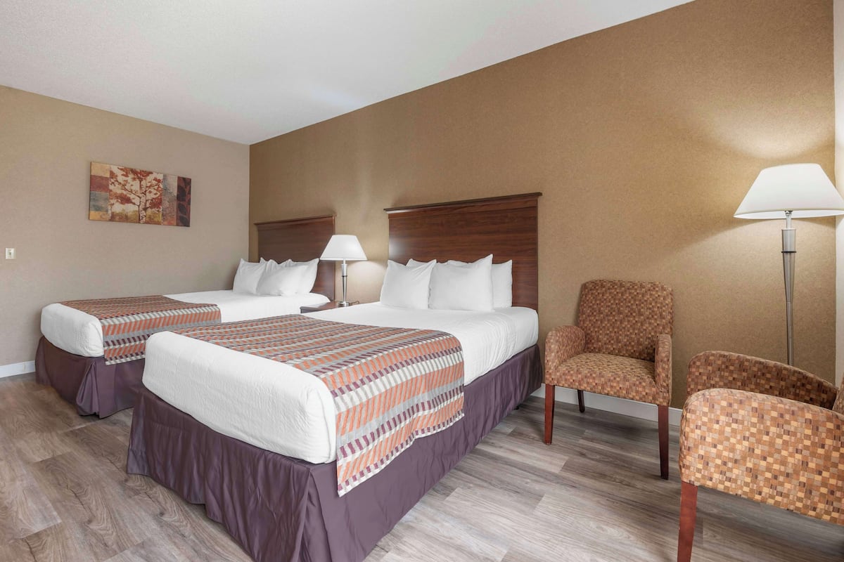 A hotel room with two beds, a chair, and a lamp.