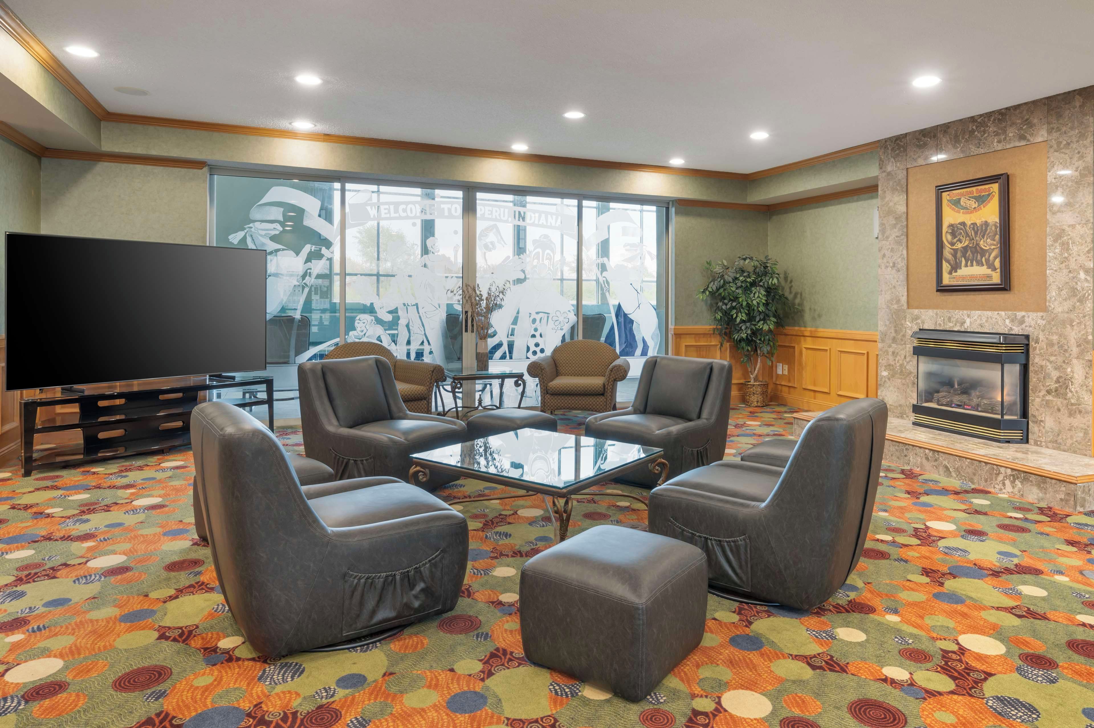 Un vestíbulo de hotel con sillones de cuero, una mesa de centro de vidrio, un televisor de pantalla plana, una chimenea y una alfombra colorida.