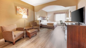 Een hotelkamer met een bed, twee fauteuils, een bureau met een televisie en een schilderij aan de muur.