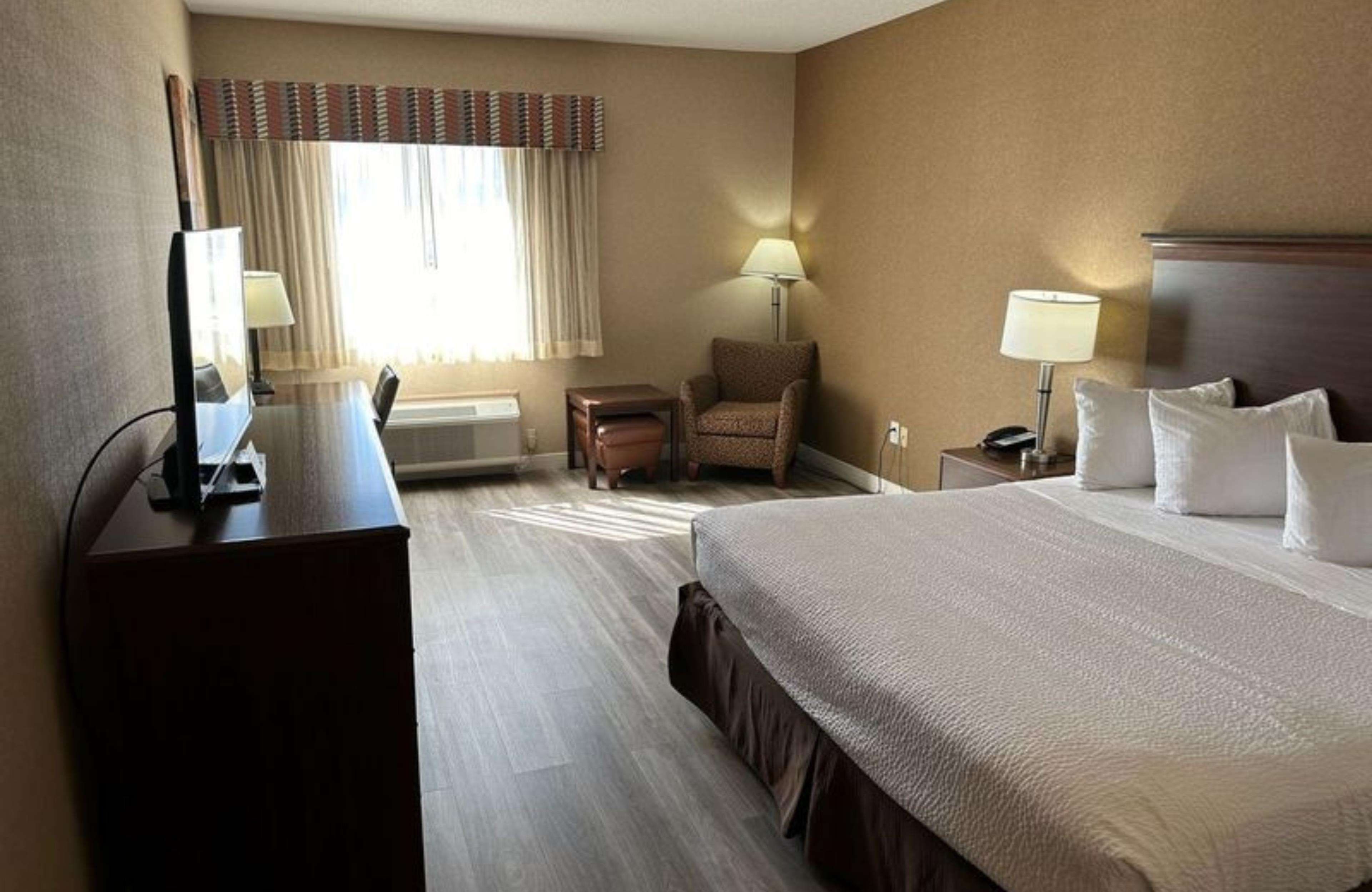 A hotel room with a large bed, a desk with a computer, a chair, two lamps, and a window with curtains.