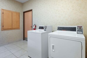 A laundry room with two white washers and dryers, a wooden door, and a fire extinguisher on the wall. - Best Western Circus City Inn (Peru)