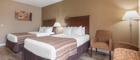 A hotel room with two beds, a chair, and a lamp.