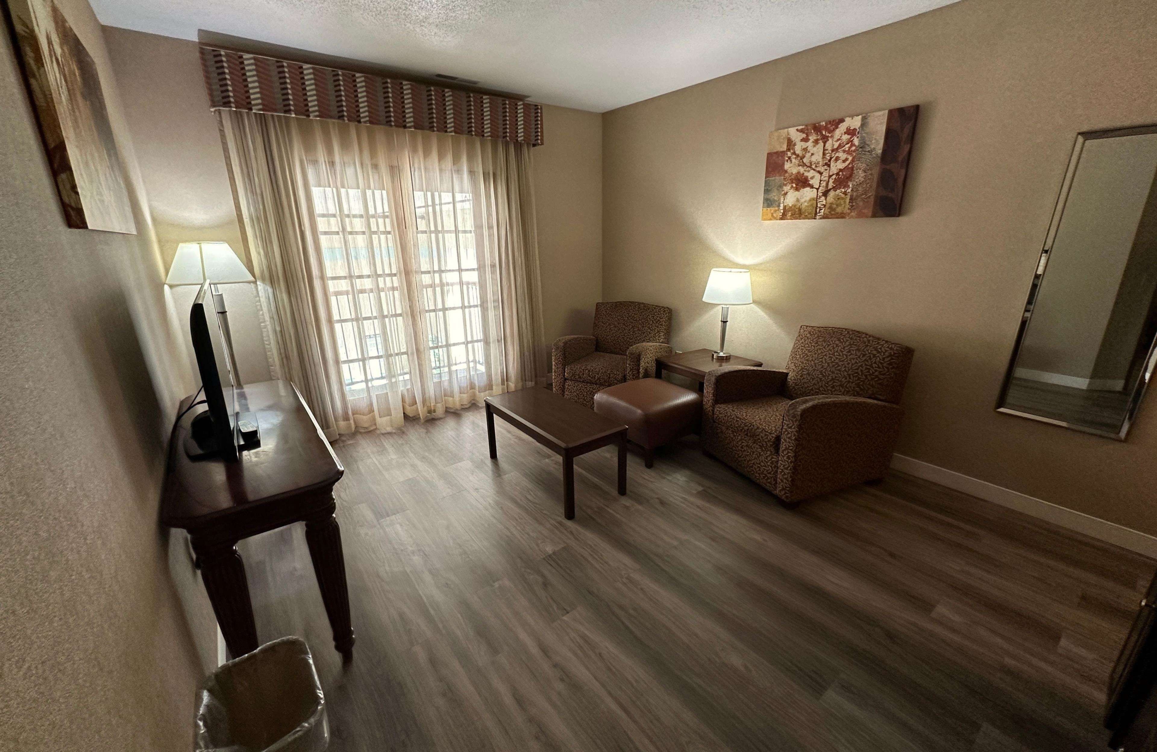 Habitación de hotel con suelo de madera, dos sillones, un sofá, una mesita, un televisor y una lámpara.