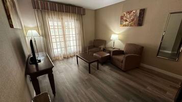Habitación de hotel con suelo de madera, dos sillones, un sofá, una mesita, un televisor y una lámpara.