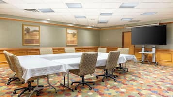 A conference room with a long table, four chairs, a projector screen, and a carpeted floor.