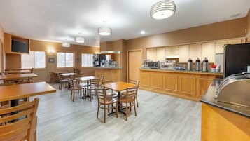A spacious dining area with wooden tables and chairs, a kitchen with wooden cabinets, and a large refrigerator.