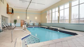 A swimming pool with a tiled deck, lounge chairs, and a small seating area.