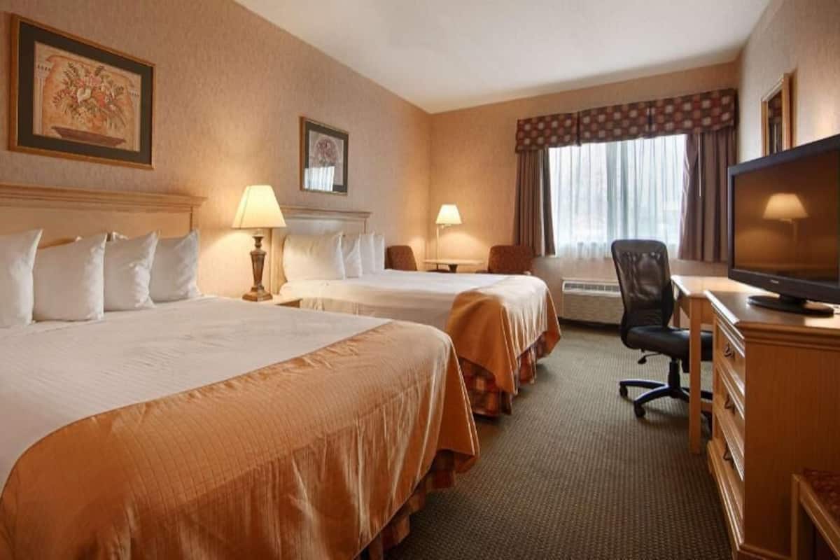 A hotel room with two beds, a desk, a chair, a television, and two lamps.