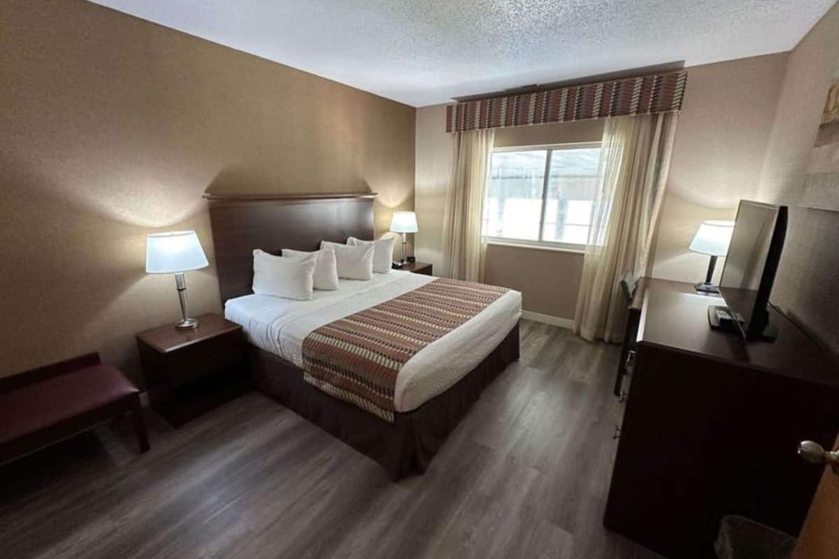 A hotel room with a large bed, two bedside tables with lamps, a dresser, and a window with curtains.