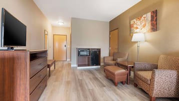 Ein Hotelzimmer mit Flachbildfernseher, einem Holzkoffer, einer Couch, einem Sessel, einem Tisch, einer Lampe und einer Mikrowelle.