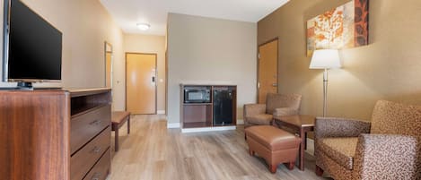 Une chambre d’hôtel équipée d’un téléviseur à écran plat, d’une commode en bois, d’un canapé, d’un fauteuil, d’une table, d’une lampe et d’un four à micro-ondes.