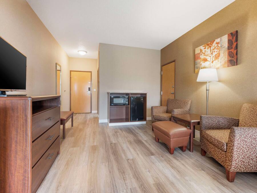 A hotel room with a flat-screen TV, a wooden dresser, a sofa, a chair, a table, a lamp, and a microwave.