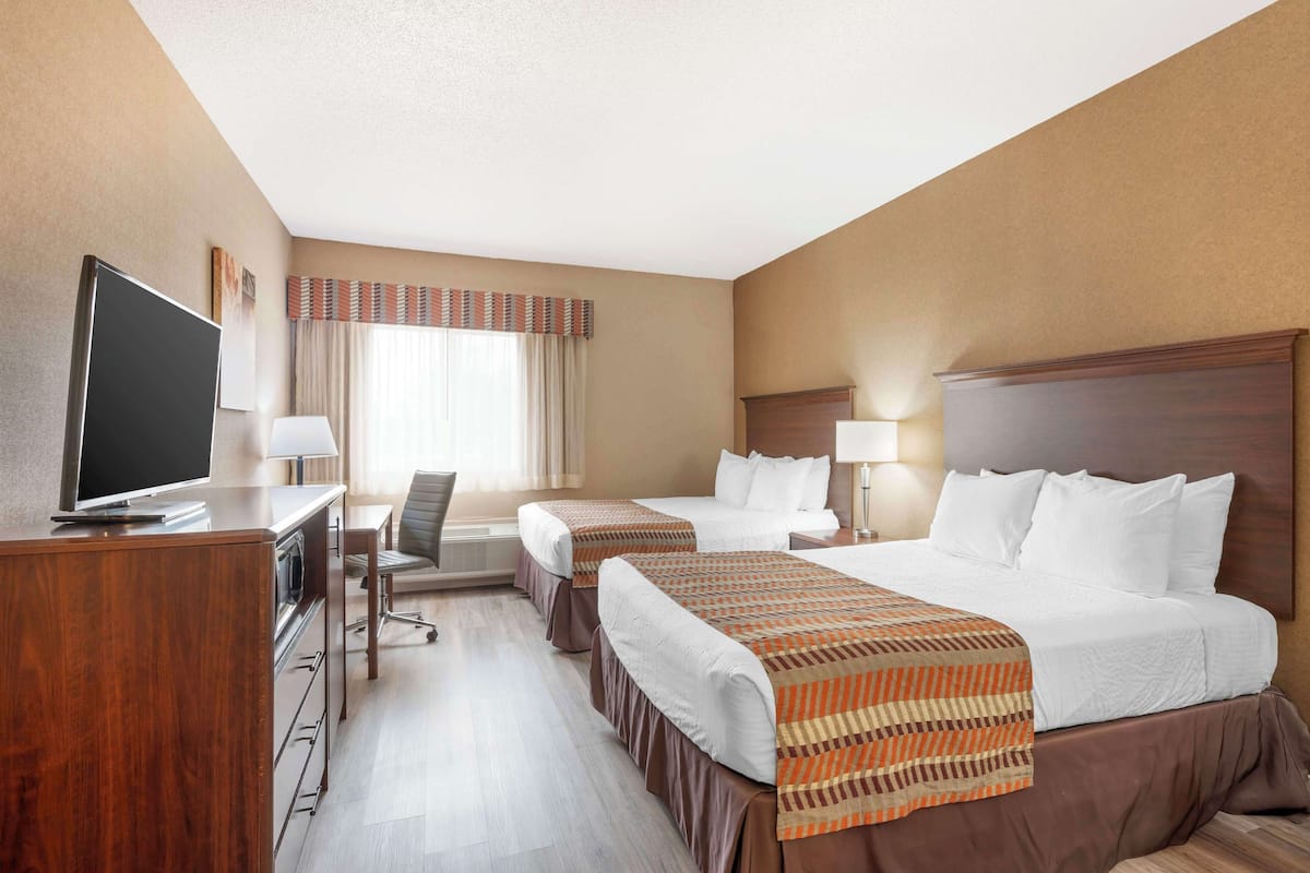 A hotel room with two beds, a desk with a TV, a chair, and a lamp.