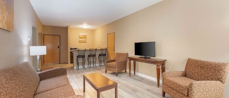 A living room with a sofa, armchairs, a coffee table, a TV, and a dining area with chairs and a table.