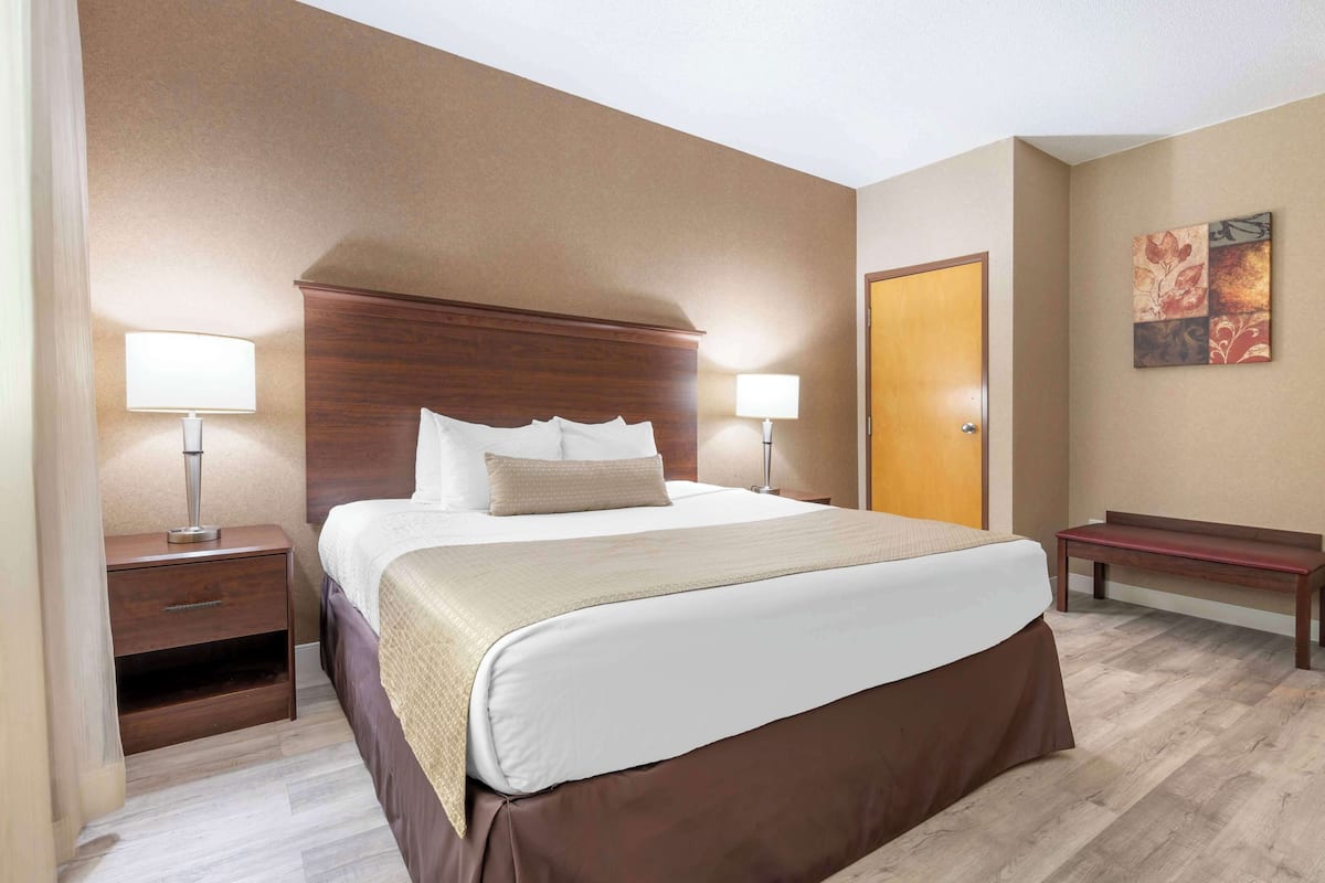 A hotel room with a large bed, two bedside tables with lamps, a wooden bench, and a door.