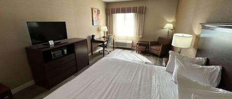 Habitación de hotel con una cama grande, un escritorio con una silla, un televisor y una ventana con cortinas.
