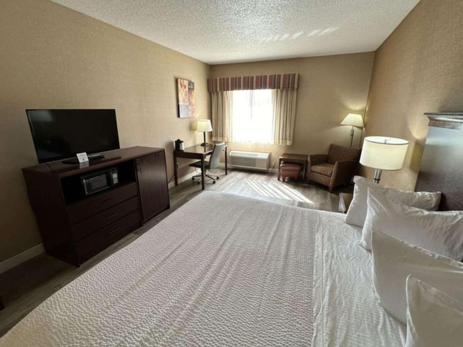 A hotel room with a large bed, a desk with a chair, a television, and a window with curtains.