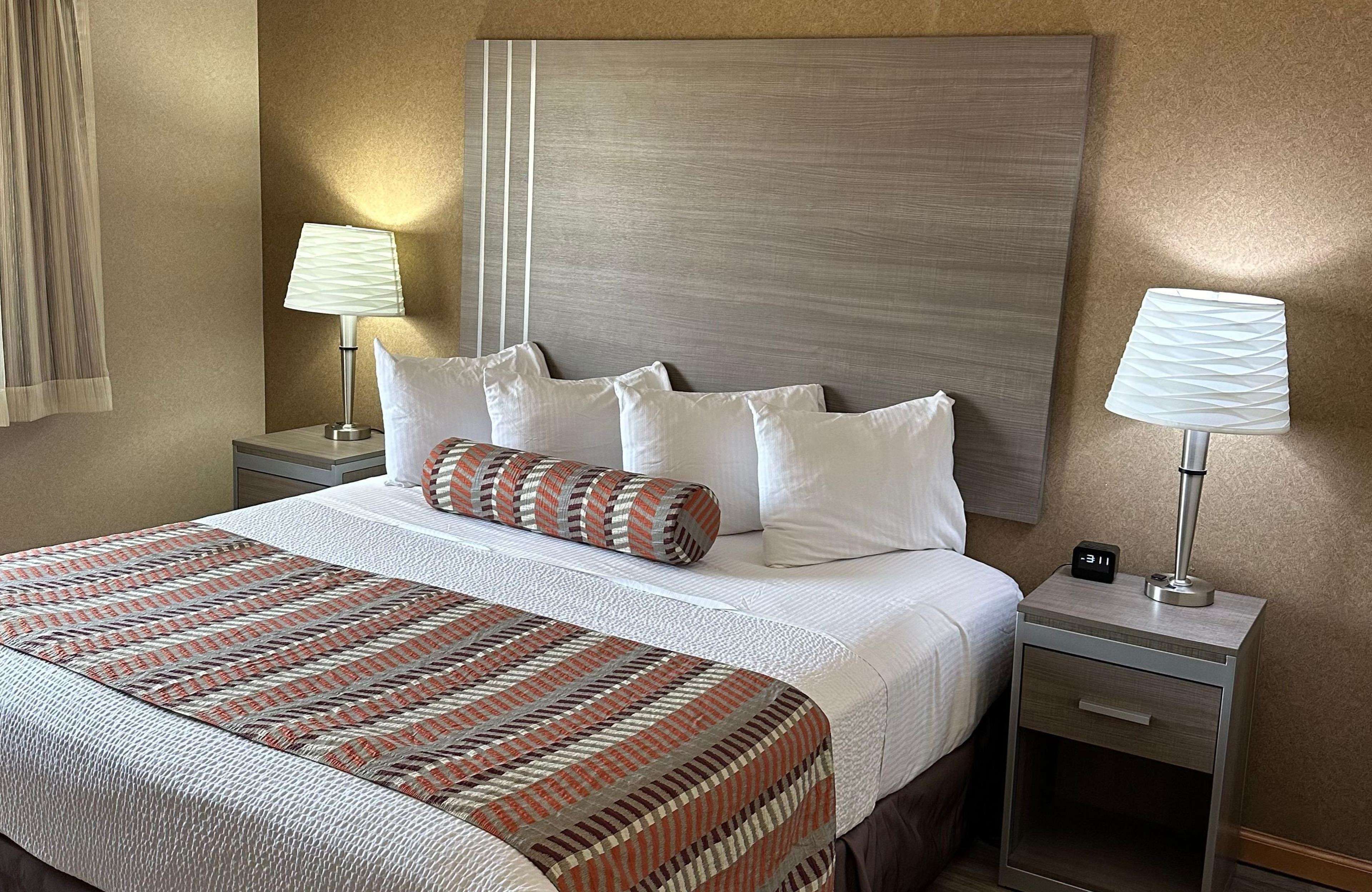 Une chambre d’hôtel avec un grand lit, deux tables de chevet, une petite table et une horloge fixée au mur.
